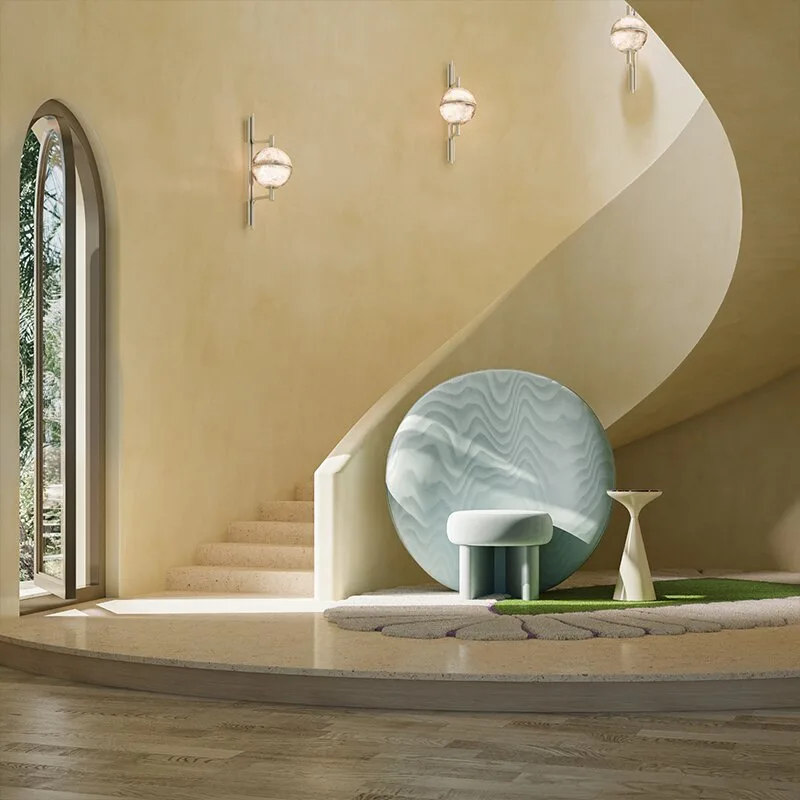Andros Wall Lamp The ice-blue Solène Armchair placed on a textured, leaf-shaped rug next to a sweeping concrete spiral staircase in a minimalist, sun-drenched Mediterranean interior with warm plaster walls. The space has 3 Andros wall lamps