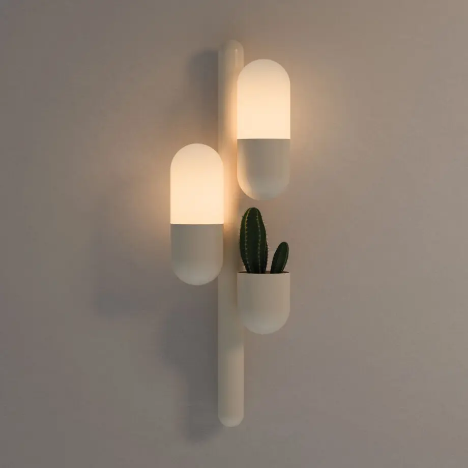 Cactus wall lamp with its two lights turned on, emitting a warm glow, lacquered in cream color with white glass shades. The piece also features a succulent plant.