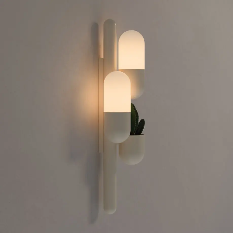 Cactus wall lamp, viewed from the side, with two lights turned on, emitting a warm glow. It is lacquered in cream color with white glass shades and features a succulent plant.