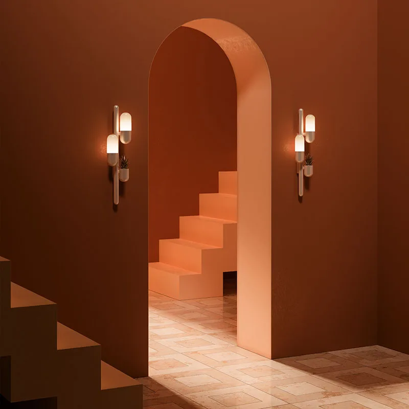 Cactus wall lamp in an orange interior. The piece has its lamps turned on, emitting a warm glow. The space features an arched entryway and stairs.