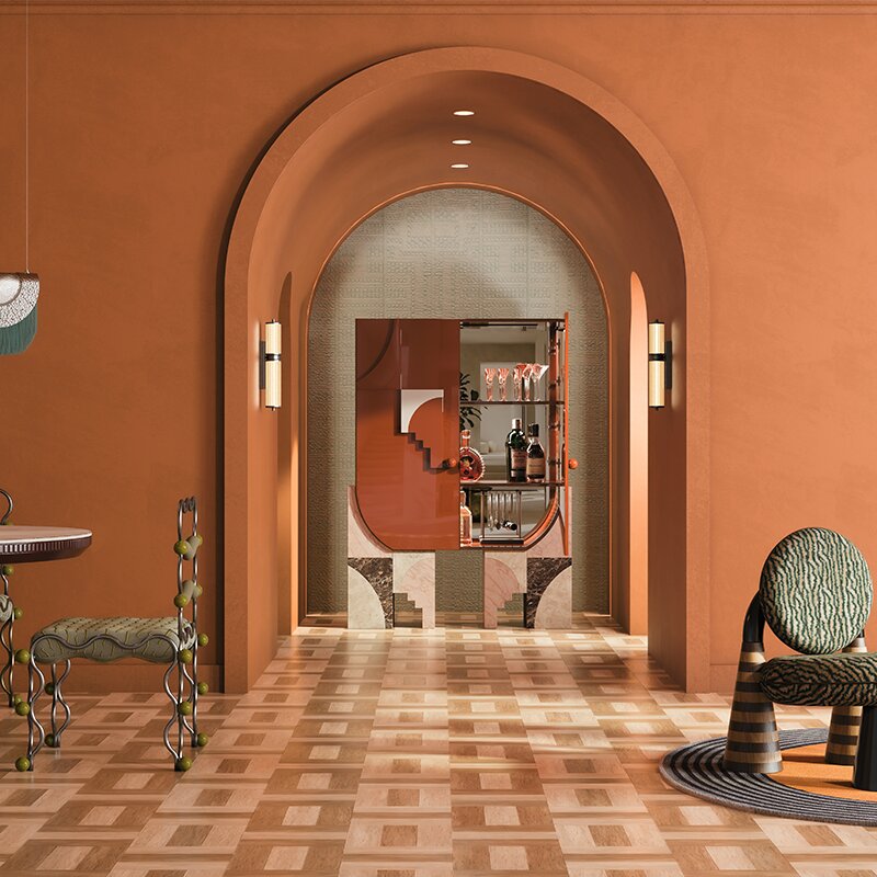 A luxurious interior with terracotta walls and a large central archway. Framed inside the arch is the open arkos bar cabinet displaying glassware, flanked by two glowing miami wall lamps. In the foreground, the uniquely styled vela dining chair sits on the left, and the totara armchair with green patterned upholstery rests on a rug to the right.